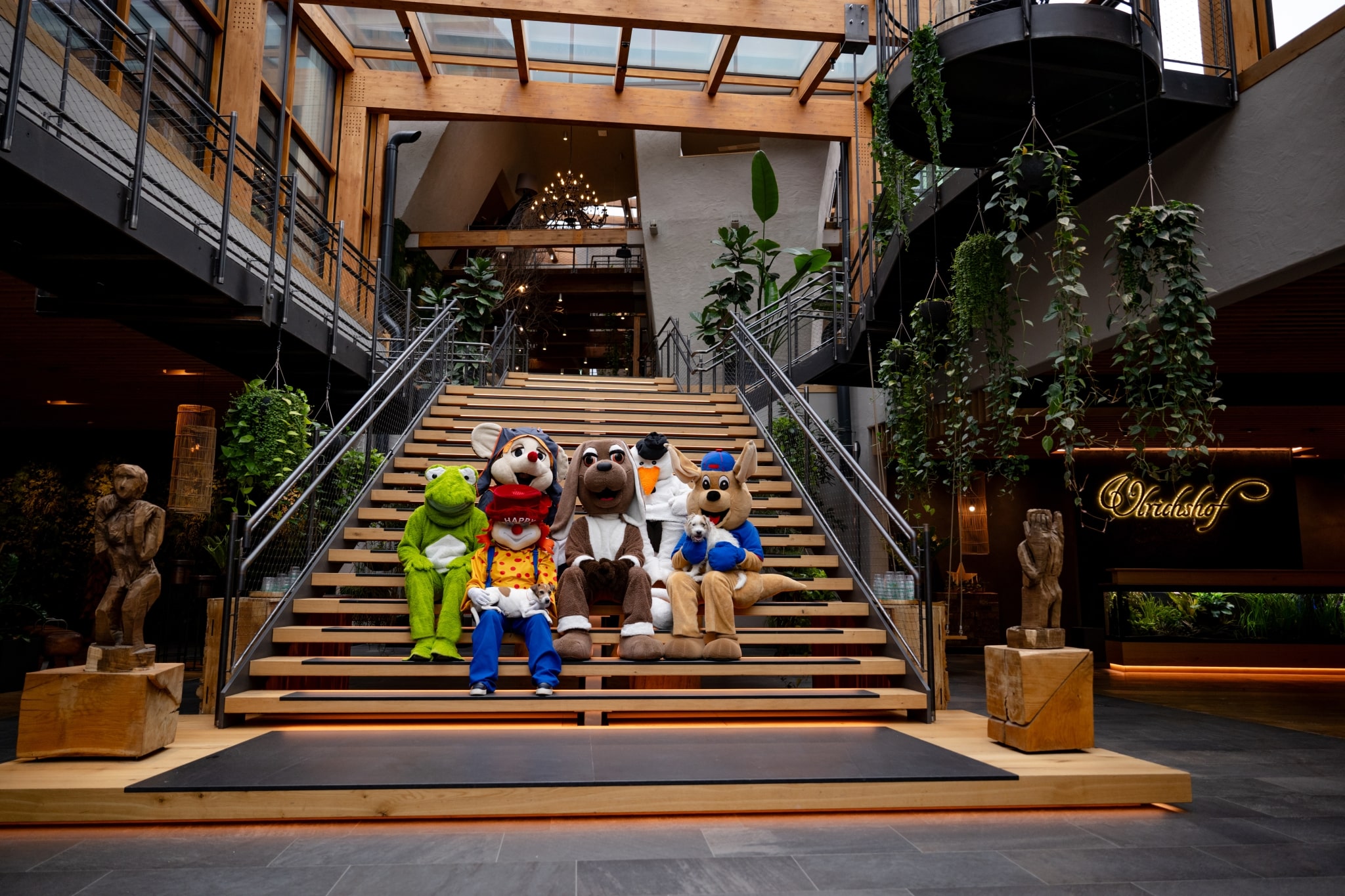 Lobby Foyer: Die ULRICHSHOF-Maskottchen nehmen Platz auf der zentralen Treppe im offenen Atrium – ein lebendiger Treffpunkt, der Natur, Design und spielerische Leichtigkeit eindrucksvoll verbindet.