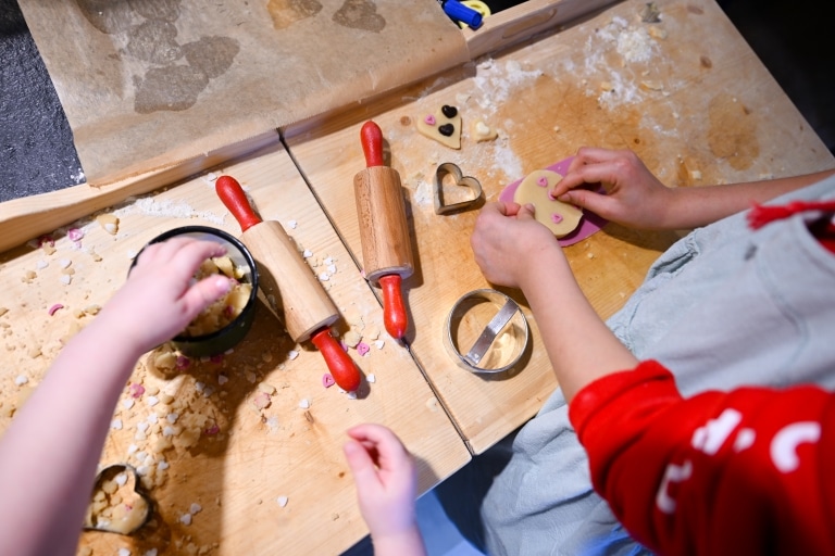 Kinder backen gemeinsam Plätzchen: Teig wird ausgerollt, ausgestochen und mit kleinen Herzmotiven verziert.