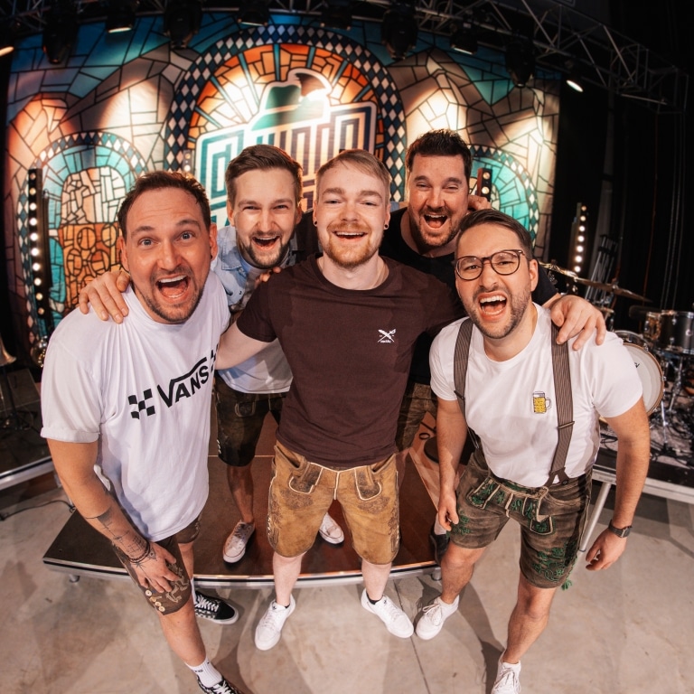Fünf Mitglieder der bayerischen Rockband D’Hundskrippln lachen fröhlich in die Kamera